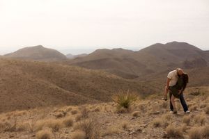 A hiker with a backpack traverses a dry, mountainous desert landscape during golden hour.