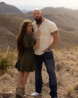 A couple poses together against a backdrop of rugged desert mountains.