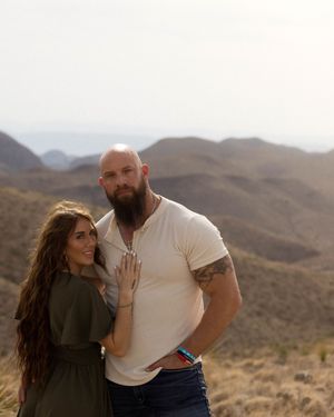 A loving couple shares a tender moment while standing in a desert landscape with mountains behind them.