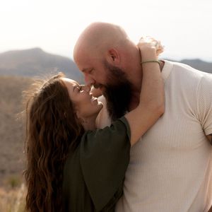 A couple share an intimate sunset moment in a desert mountain landscape, silhouetted against warm golden light.
