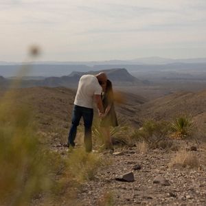 A couple shares a romantic moment on a desert mountain overlook during sunset.