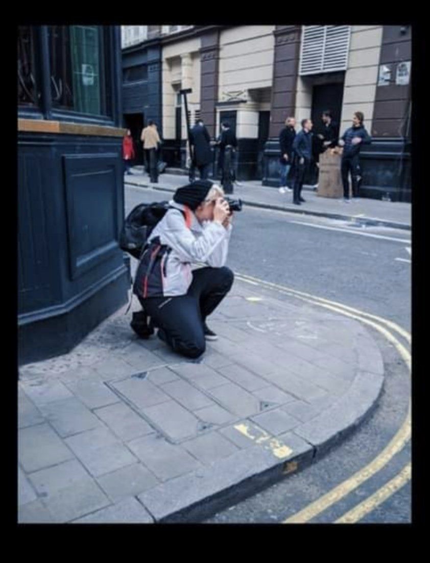 Photographer in casual attire crouching on street corner to capture urban scene.