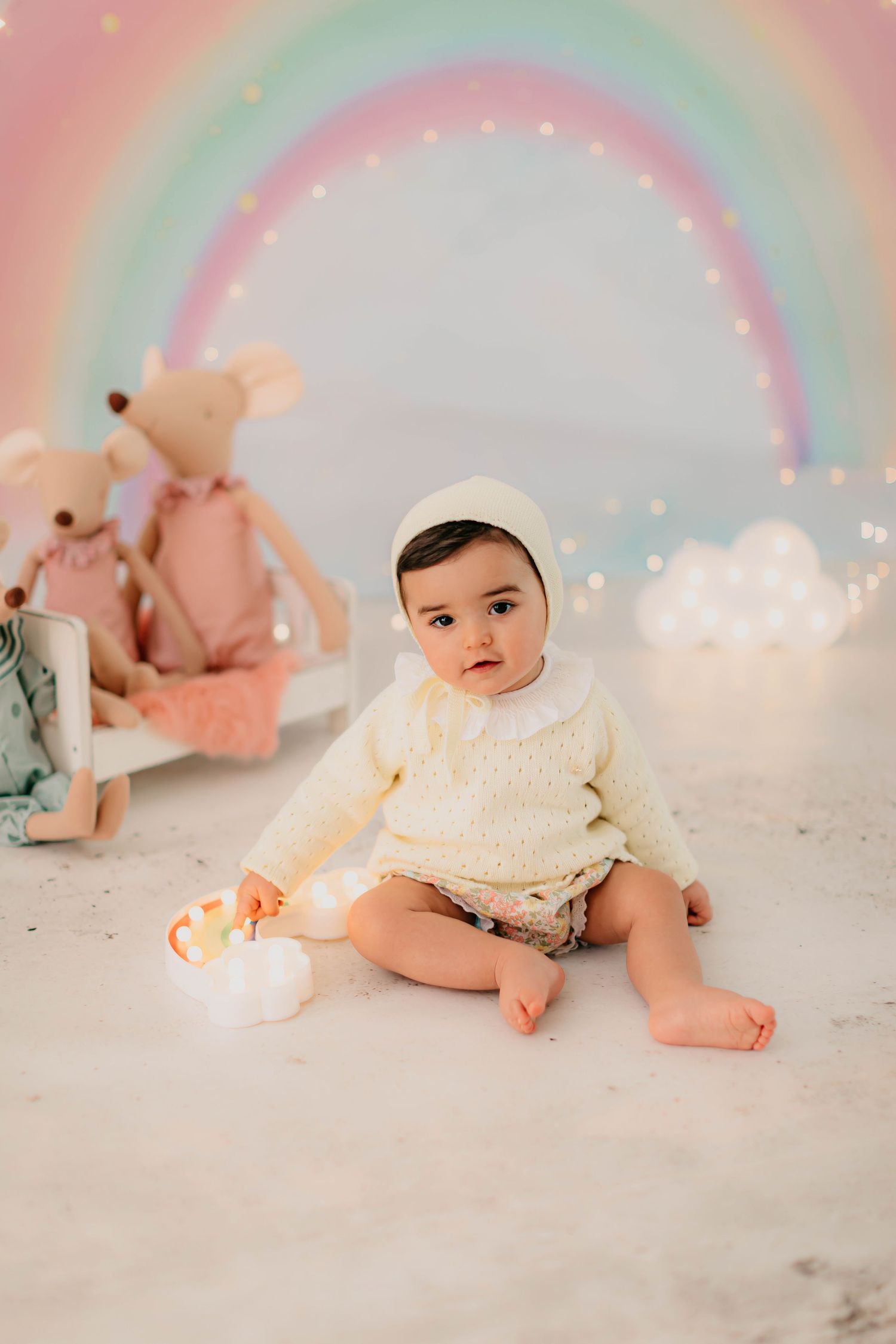 Niña de seis meses vestida con conjunto en amarillo claro y fondo de arcoiris en una sesión fotográfica de seguimiento.
