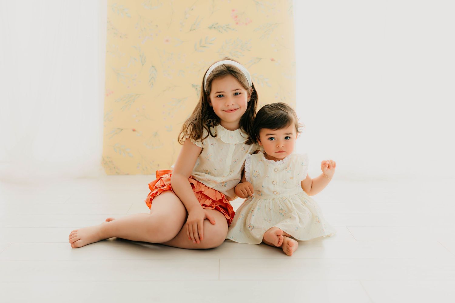 Fotografía de una bebé de un año junto a su hermana mayor en una sesión fotográfica de seguimiento.