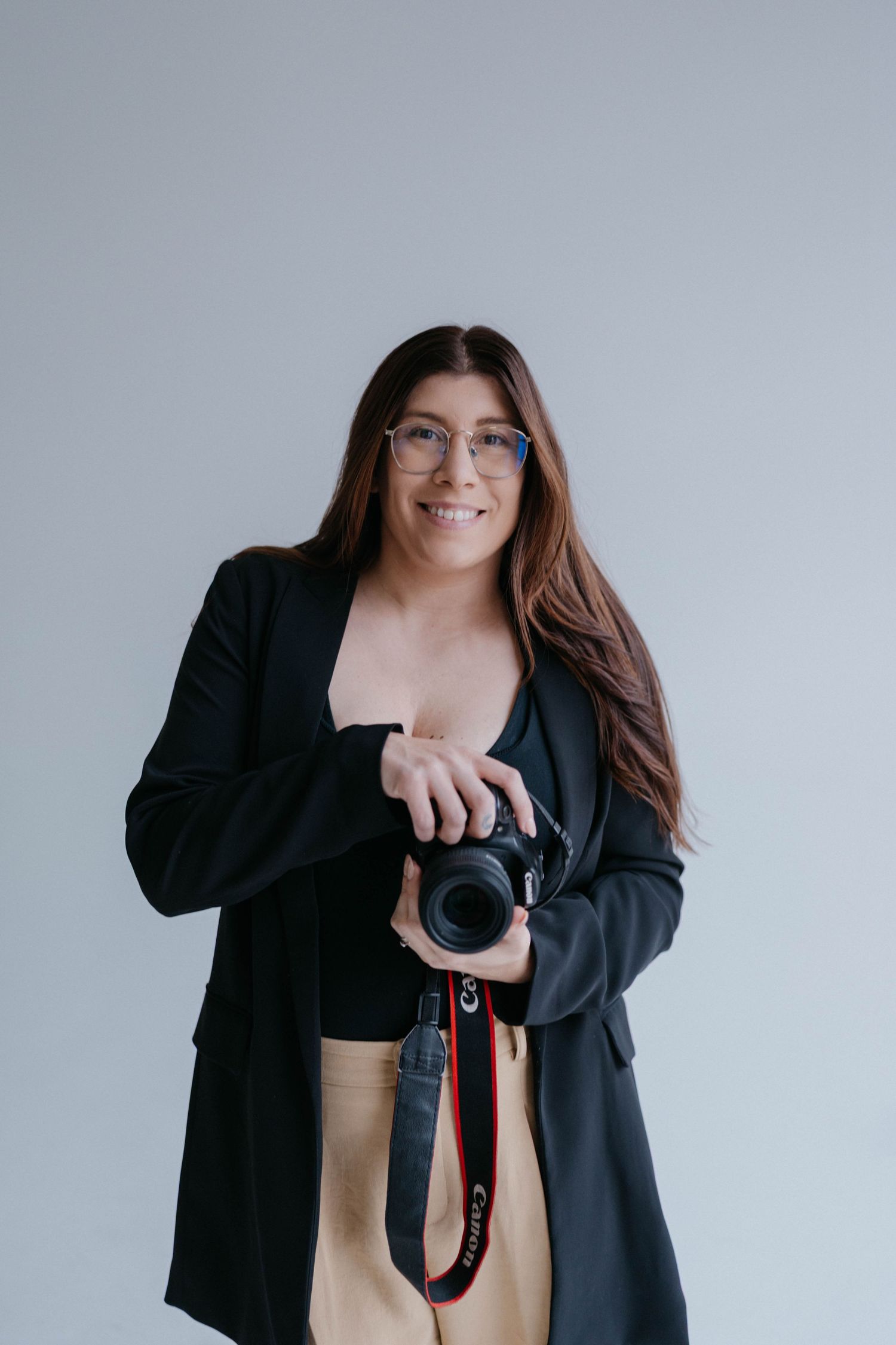 Antonella, Colorado's Photographer in a black jacket and jeans holds a professional camera against a white background. Photographer portrait