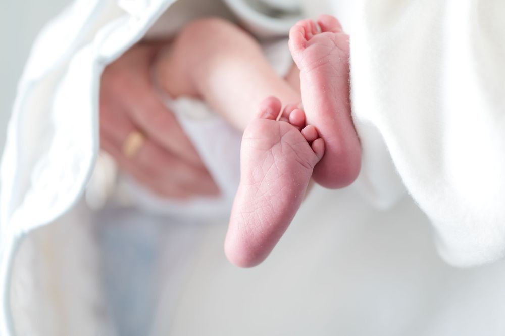 Close-up of tiny pink newborn baby feet against white fabric background.