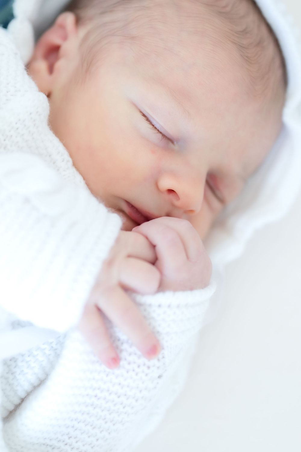 A peaceful sleeping baby wrapped in a soft white knitted blanket.