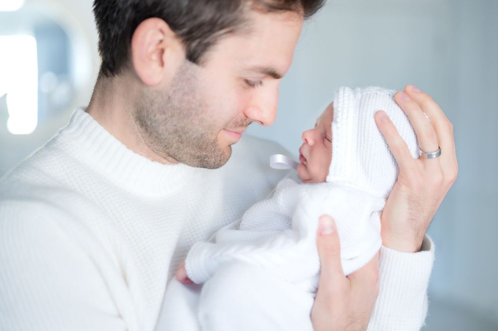A gentle moment between parent and newborn baby wrapped in white blanket.