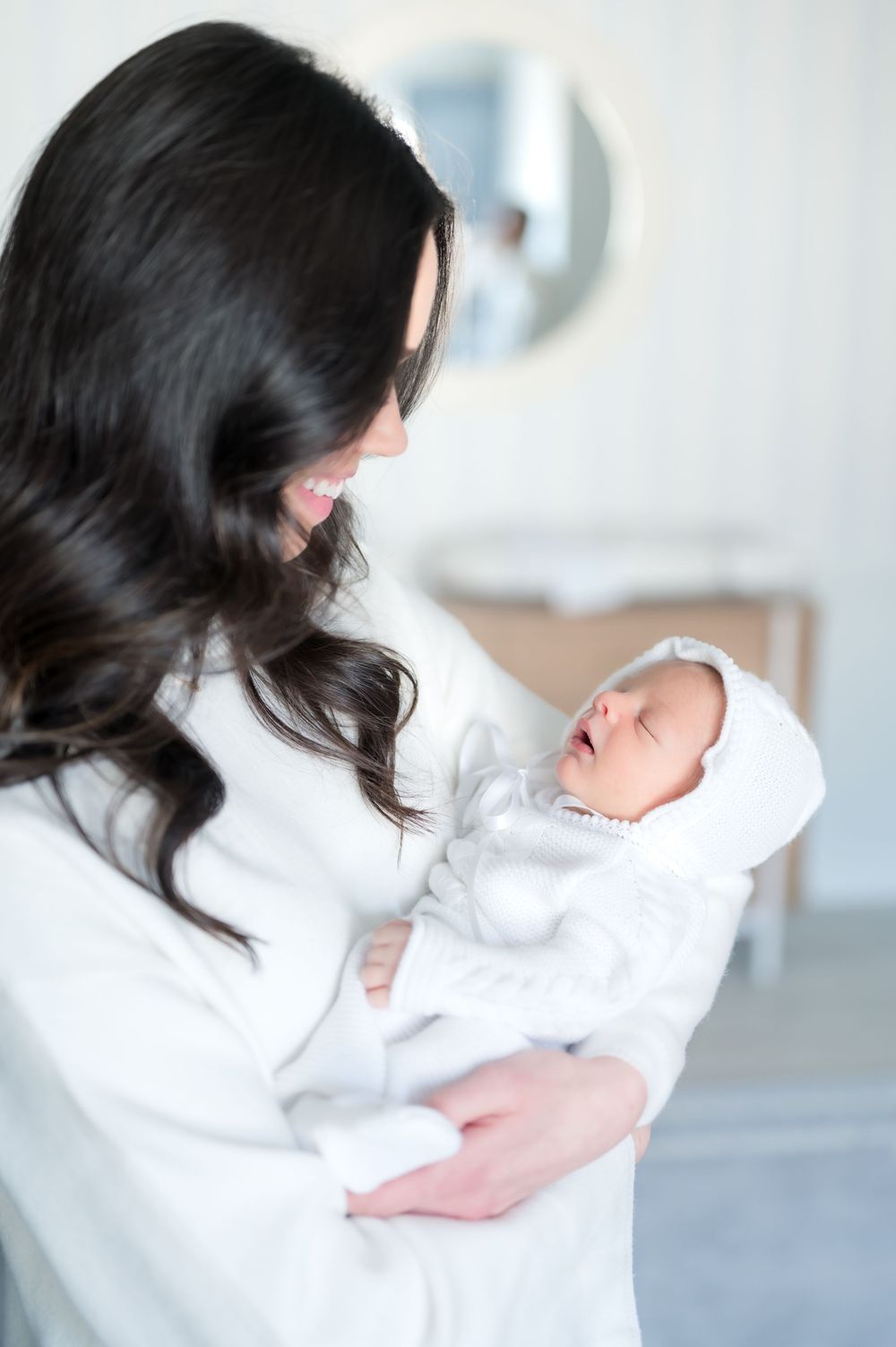 A tender moment between parent and newborn baby wrapped in white, captured in soft natural light.