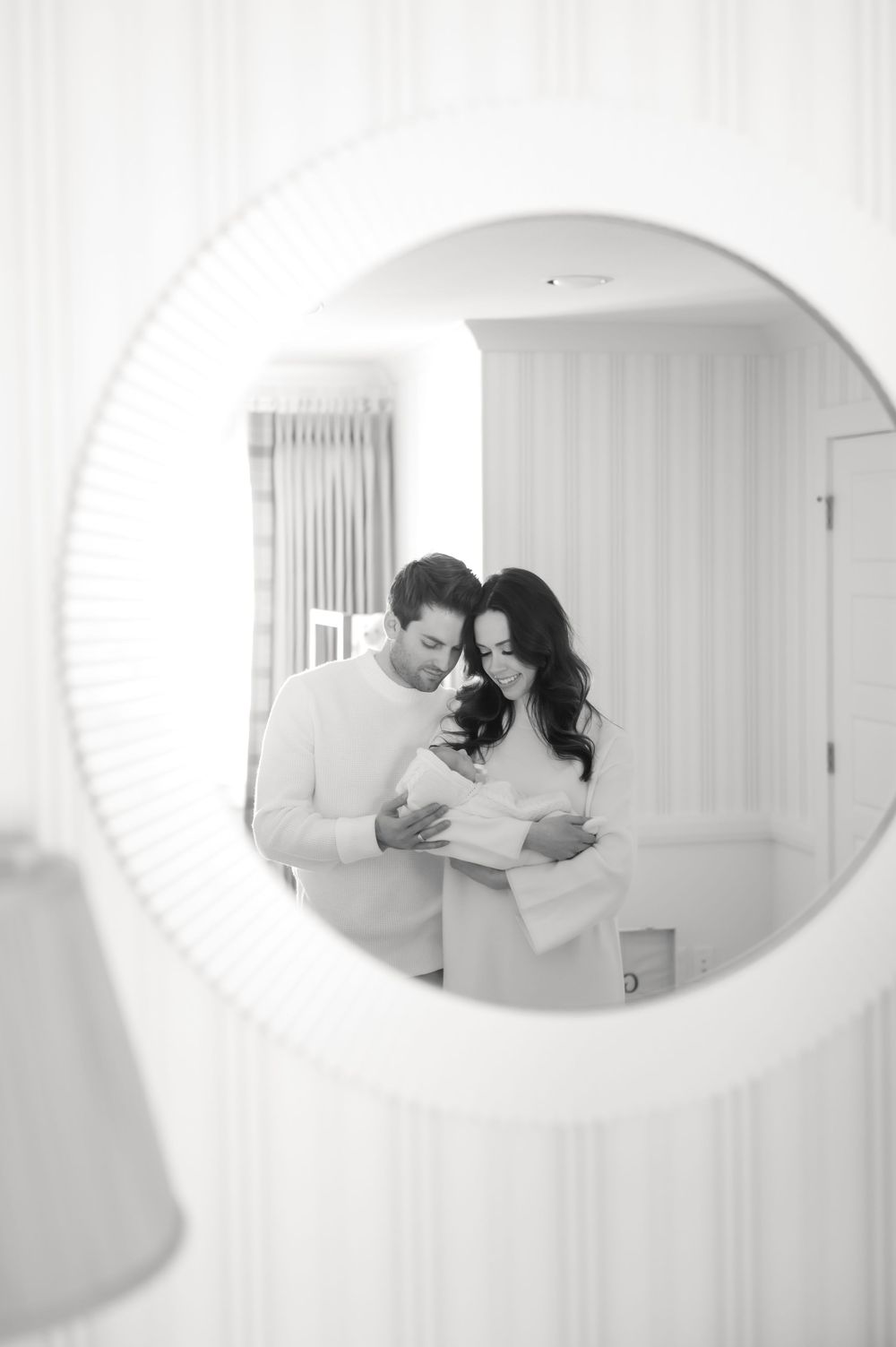 A couple shares an intimate moment while reading papers together, viewed through a round mirror frame in a white interior.