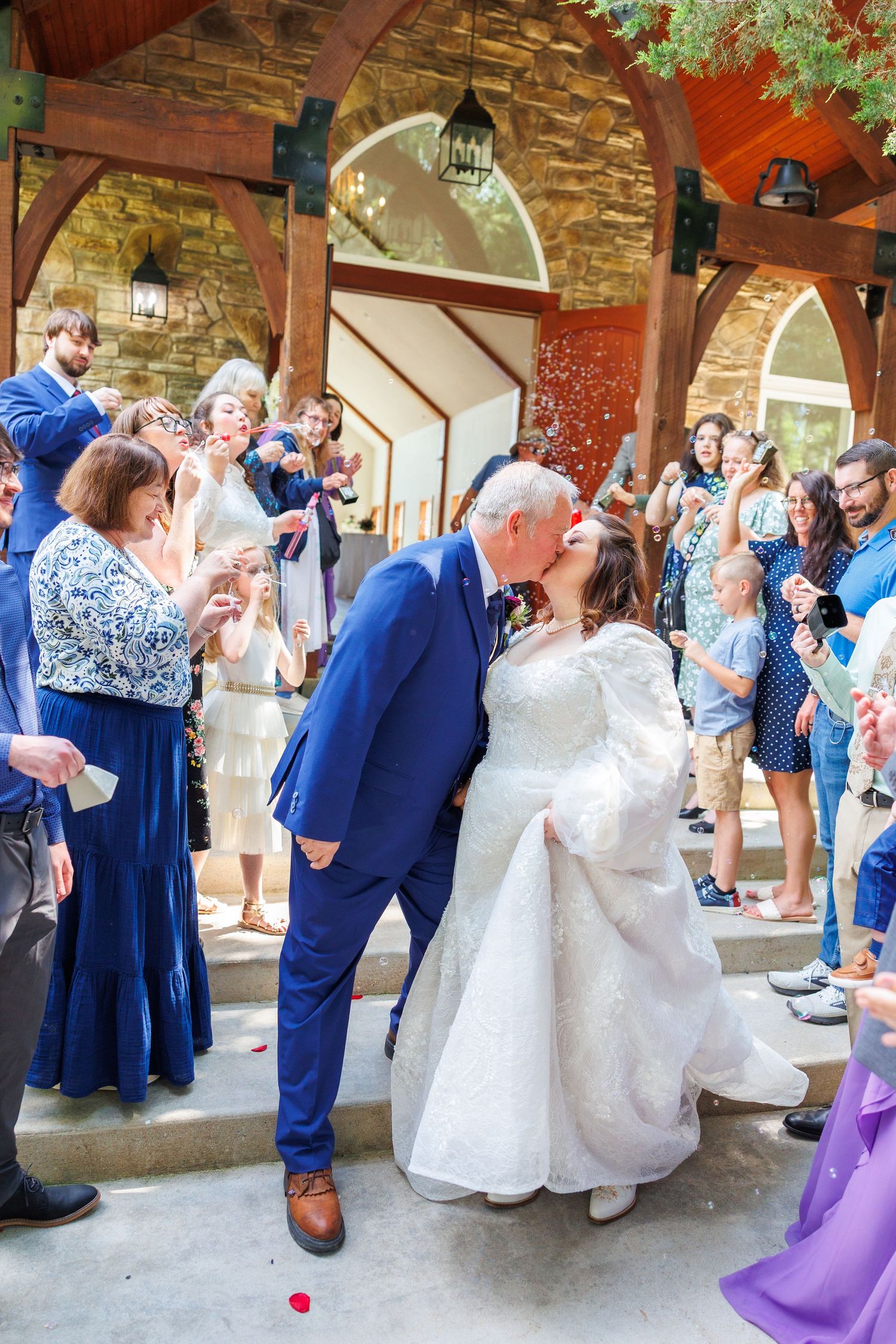 Joyful wedding moment captured under stone arches as guests shower the couple with red petals.