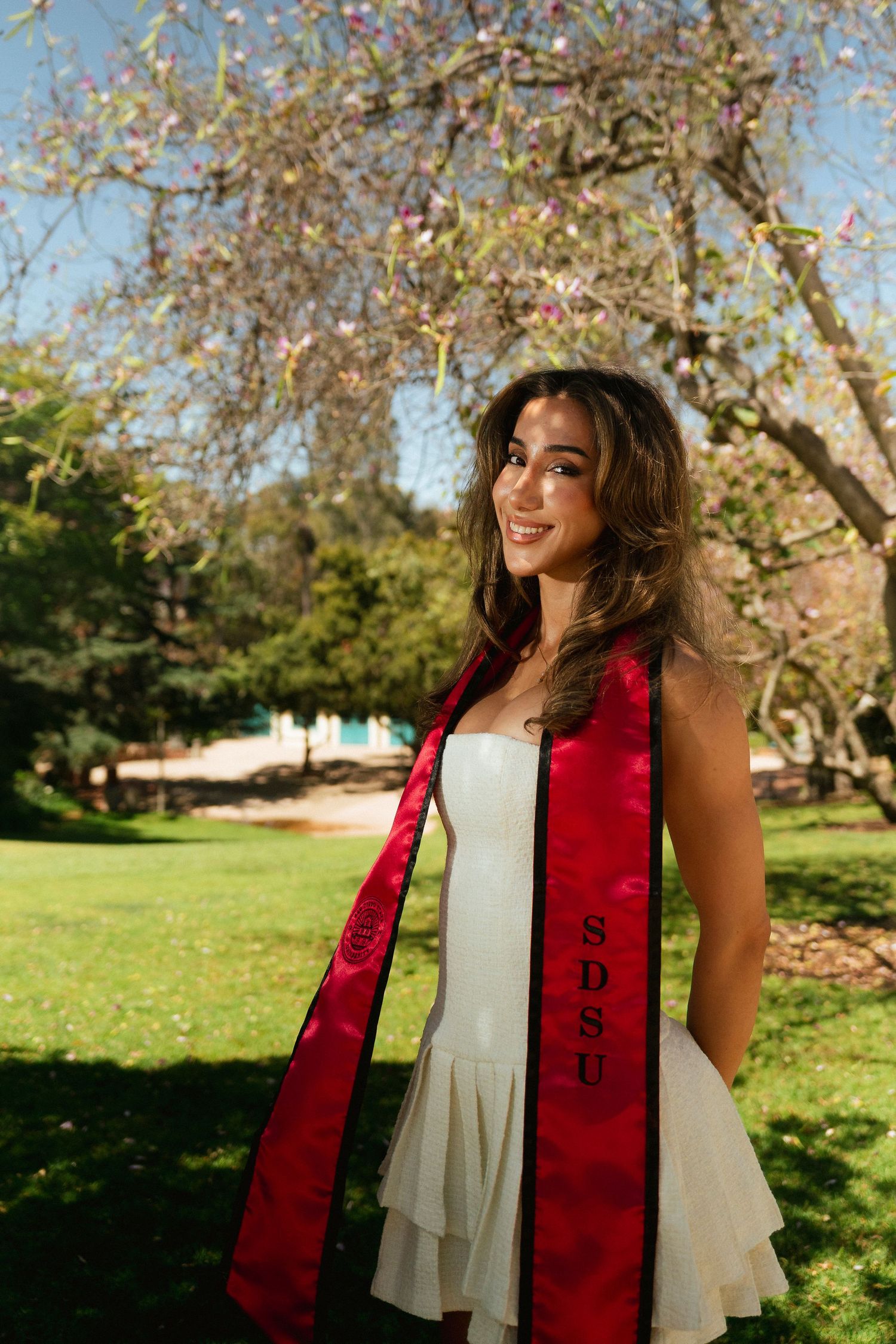 A young woman poses in an open field surrounded by green trees