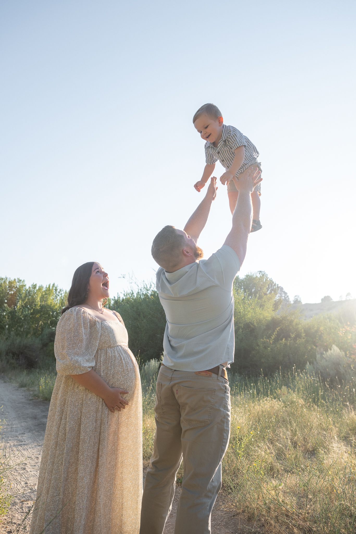 A father plays with his son in the evening sun while the mom looks on. Taken during maternity and family photos in the foothills of Boise