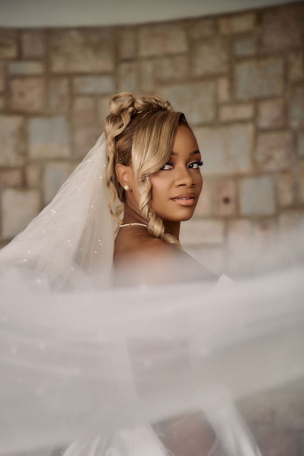 Beautiful bride in flowing white veil poses against stone wall background in romantic wedding Jamaica Wedding Photographer