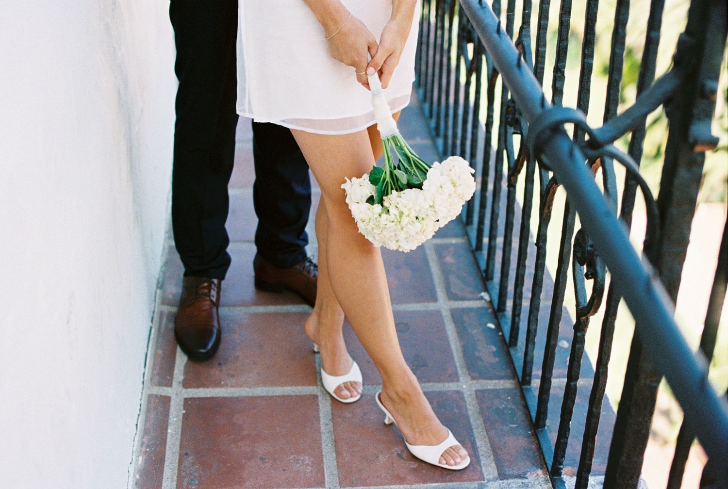 Wedding party members in formal attire walk together across an outdoor pathway with railings.