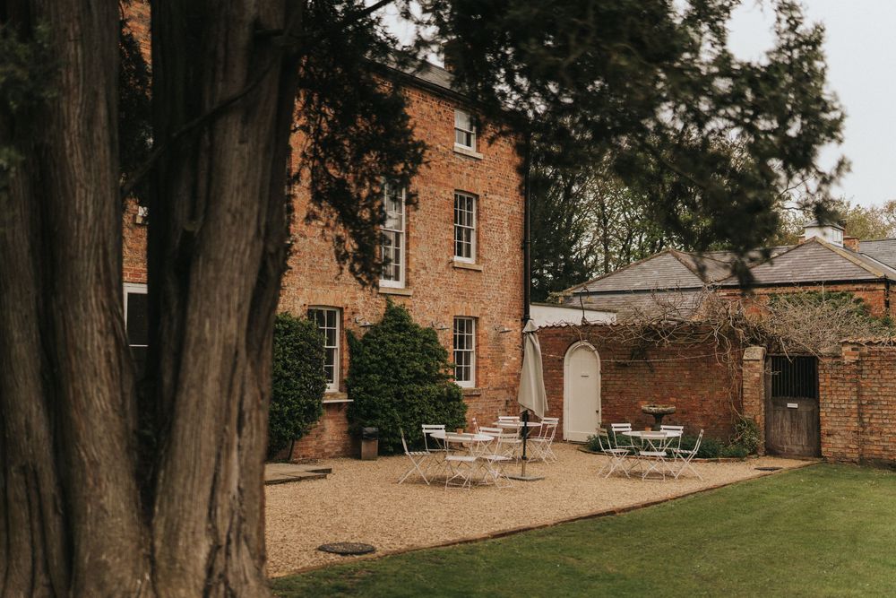 Historic brick buildings line a path with green lawn and mature trees at Aswarby Rectory.