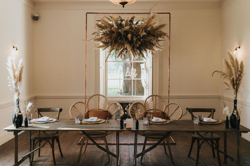 Minimalist dining table set with dried floral arrangements and copper chairs in a neutral-toned room with wall sconces at Aswarby Rectory.