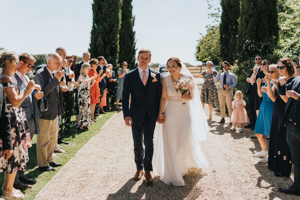 Wedding guests form a joyful walkway in bright summer sunlight as people walk through the line of well-wishers.