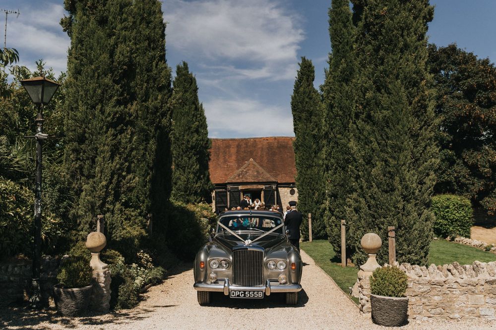 A Mercedes-Benz car parked in a scenic driveway lined with tall cypress trees under a blue sky with clouds.