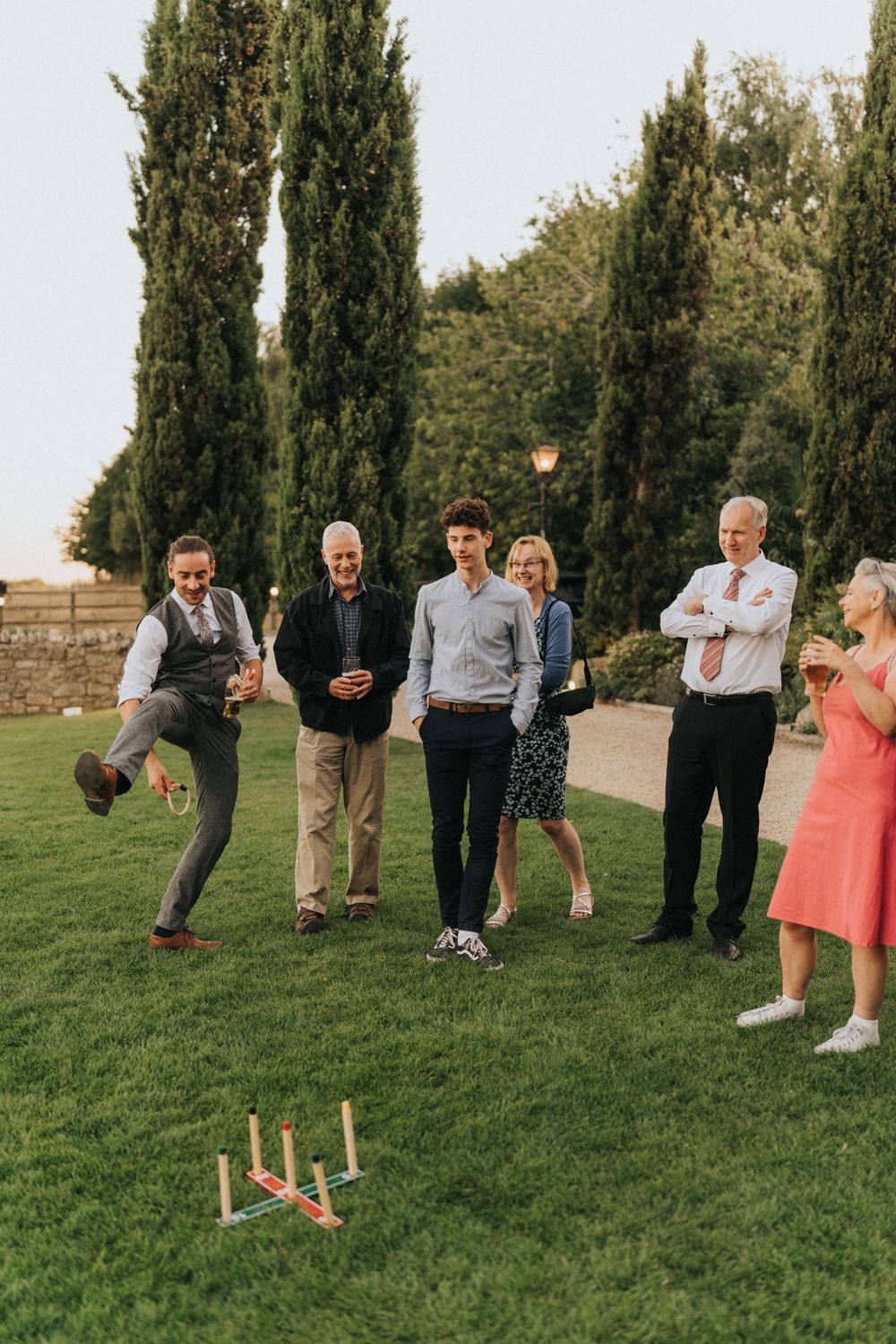 Group playing a lawn game with ring toss on green grass with cypress trees in the background during outdoor gathering.