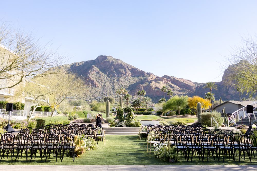 Dark wooden chairs arranged in rows for an outdoor wedding ceremony with dramatic mountain peaks in the background.