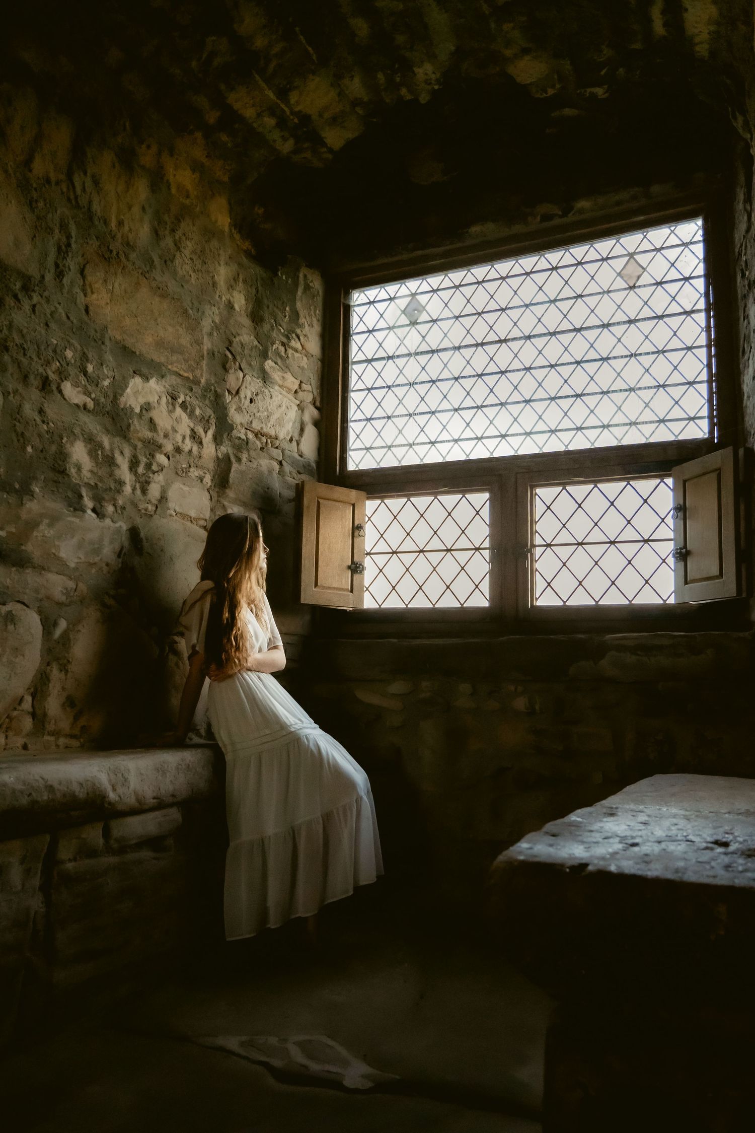 young women sits next to a window in a castle in the glow of light