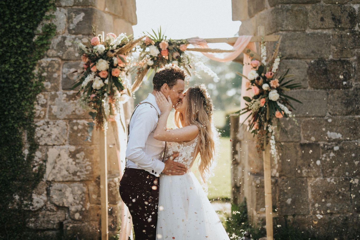 Newlywed couple shares a romantic kiss in a bright church setting surrounded by wedding guests and blush-toned decor.