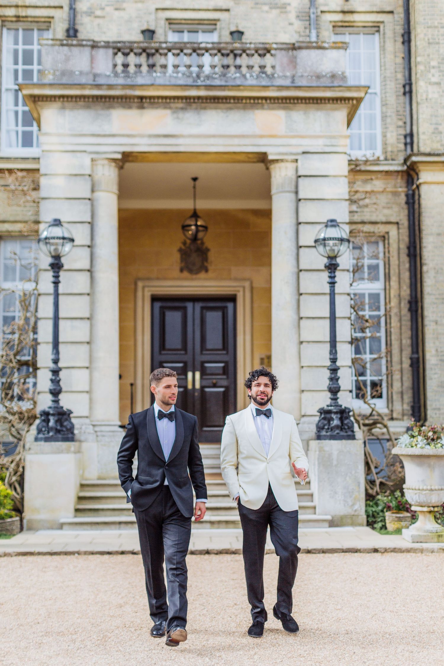 Groom and best man walk together outside Hedsor House with ornate stone architecture and lamp posts. London wedding photographer
