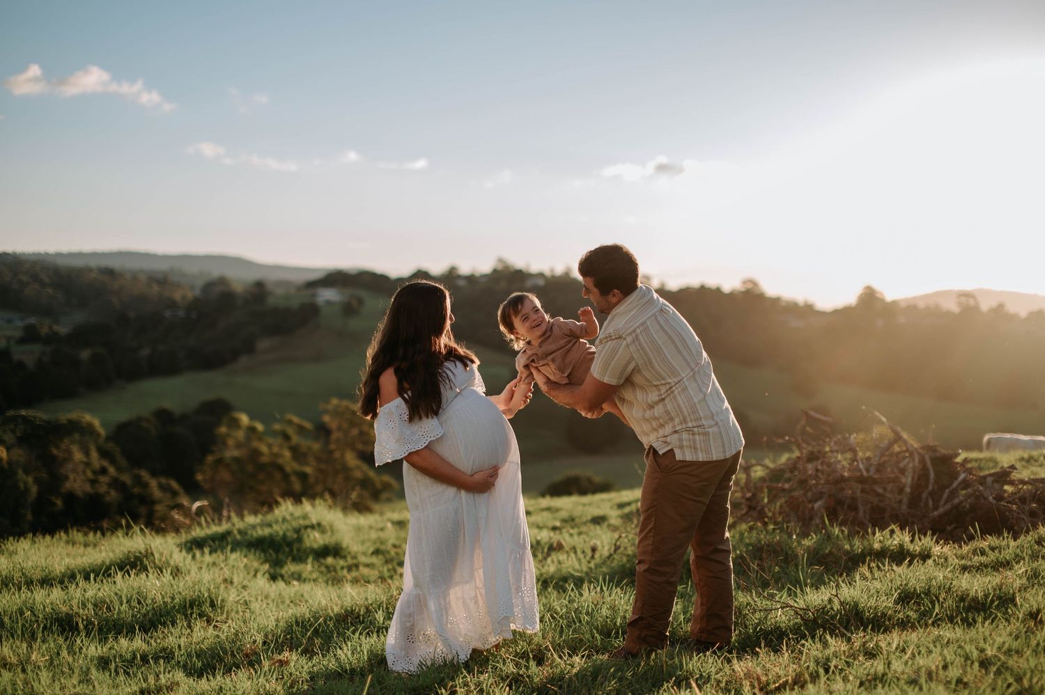A scenic hilltop at sunset features a family enjoying a tender moment together in a grassy meadow.