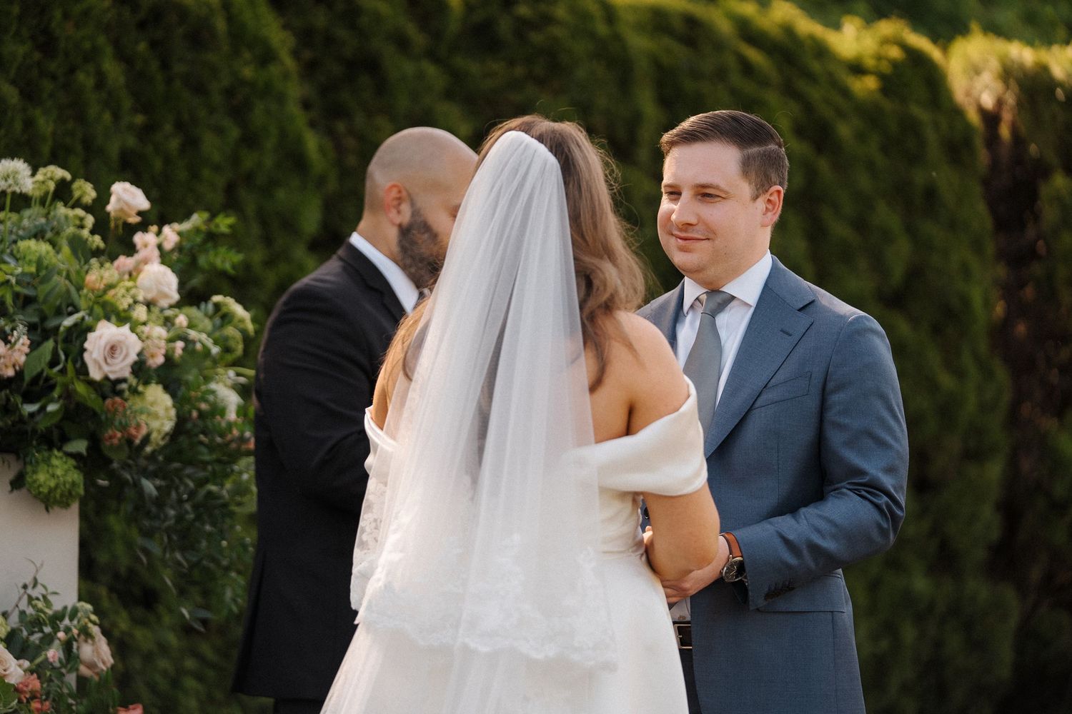 An elegant outdoor wedding ceremony takes place in a beautiful garden setting surrounded by lush greenery.