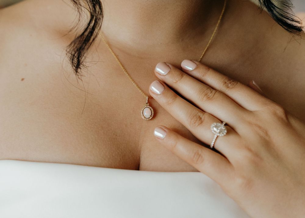 Close up of hands wearing elegant diamond rings with white nail polish against bare skin and white fabric.