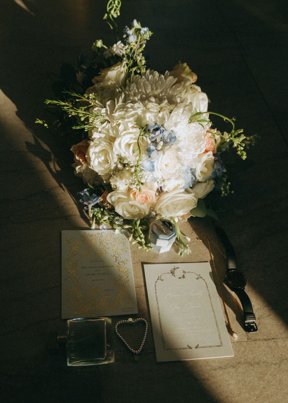 Wedding bouquet of white roses with eucalyptus alongside vintage stationery and a heart charm in dramatic lighting.