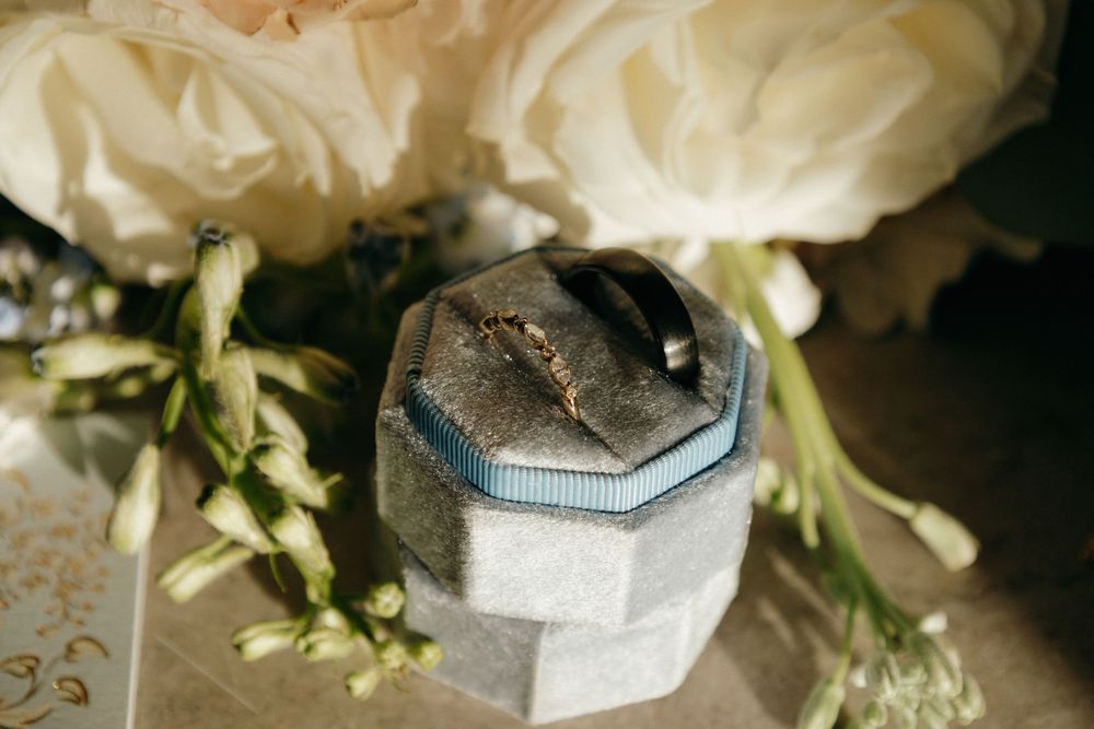 Wedding rings displayed in an elegant octagonal box surrounded by white roses and greenery.
