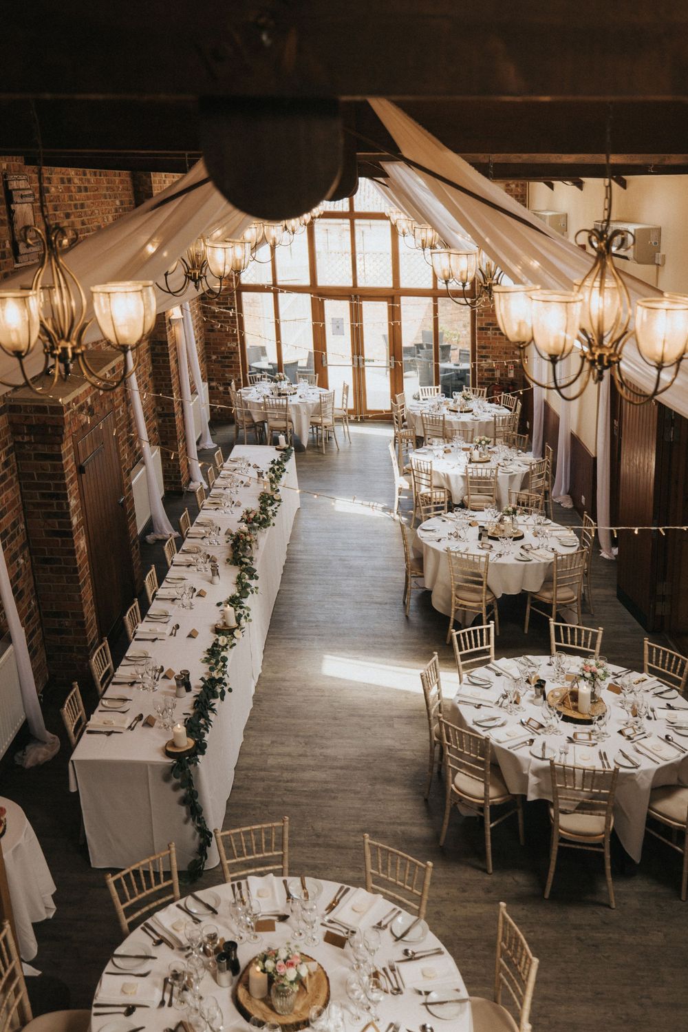 Elegant rustic wedding reception venue with wooden beams, chandeliers, and round tables at Hall Farm - captured by Grimsby photographers.