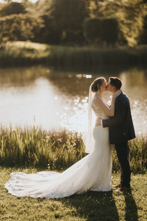 Romantic wedding couple shares intimate moment by sunlit lake at Hall Farm - image captured by Grimsby photographers.