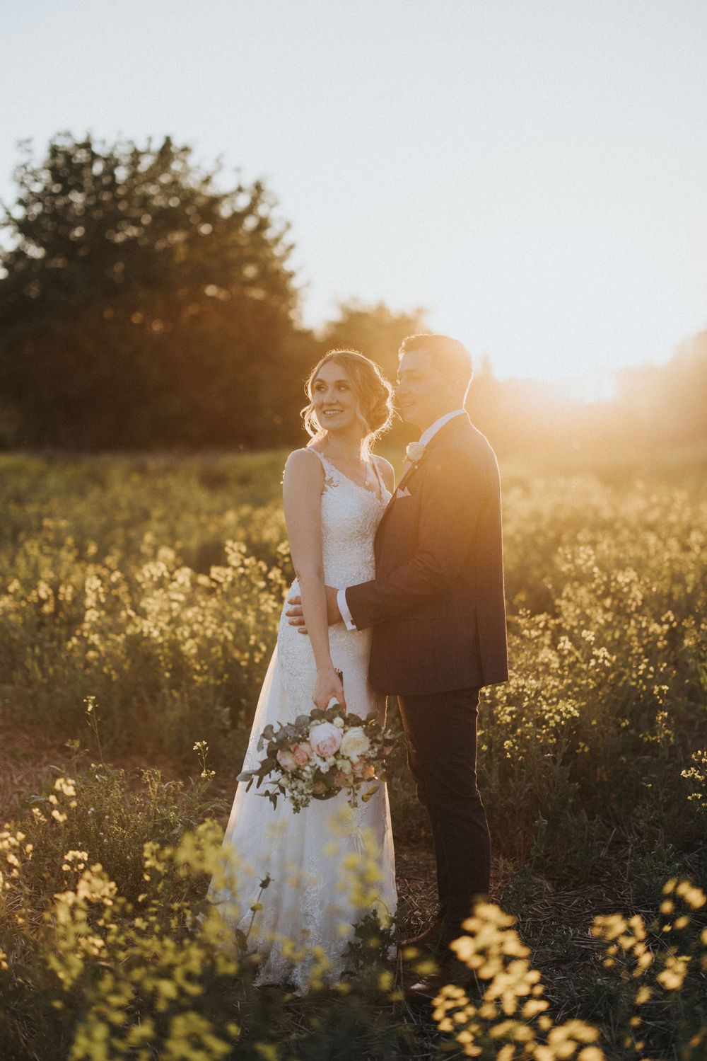 A couple shares a romantic moment in a sunlit field during golden hour at Hall Farm - image captured by Grimsby photographers.