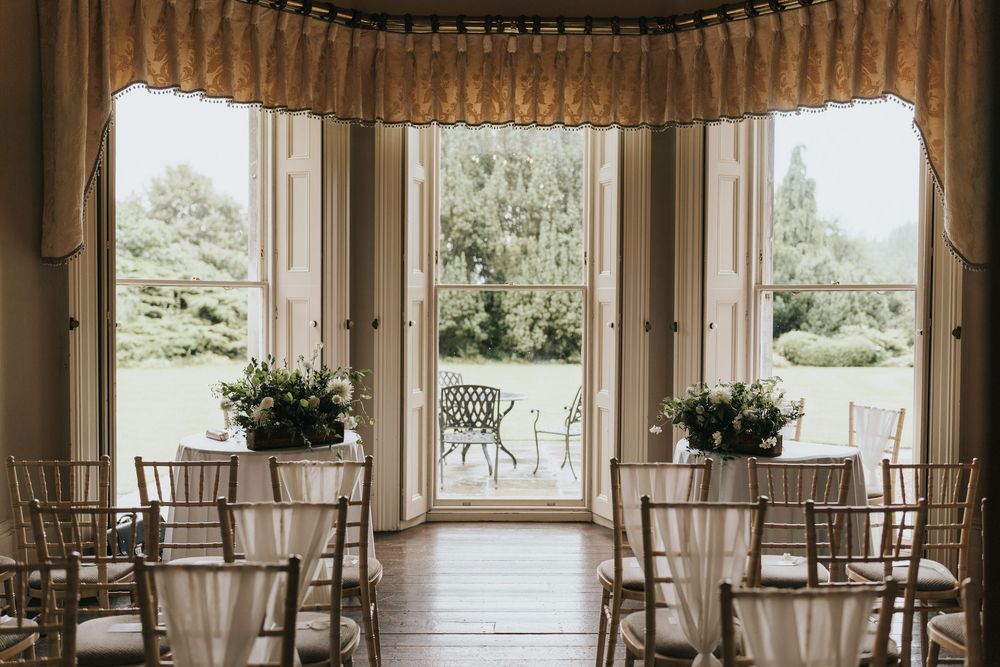 Elegant bay window wedding ceremony setup with chiavari chairs and potted floral arrangements at Cleatham Hall.
