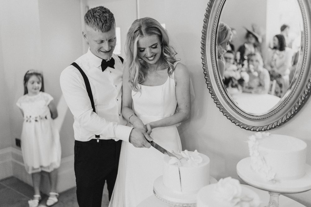 Black and white candid photo of a wedding couple cutting their cake together while a young girl watches in background at Cleatham Hall.