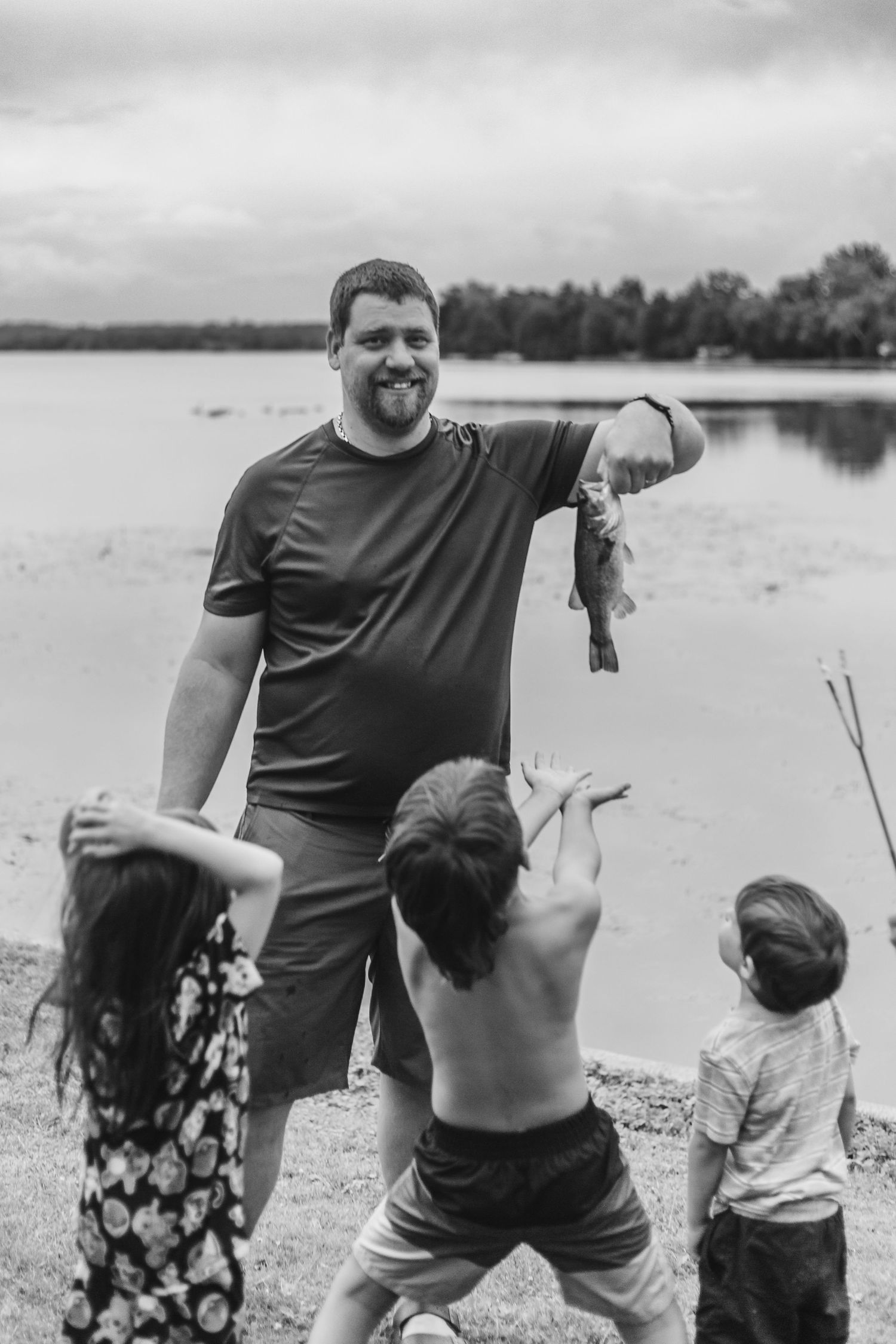 Children celebrating a successful fishing catch at a lakeside with parent on a summer day in black and white.