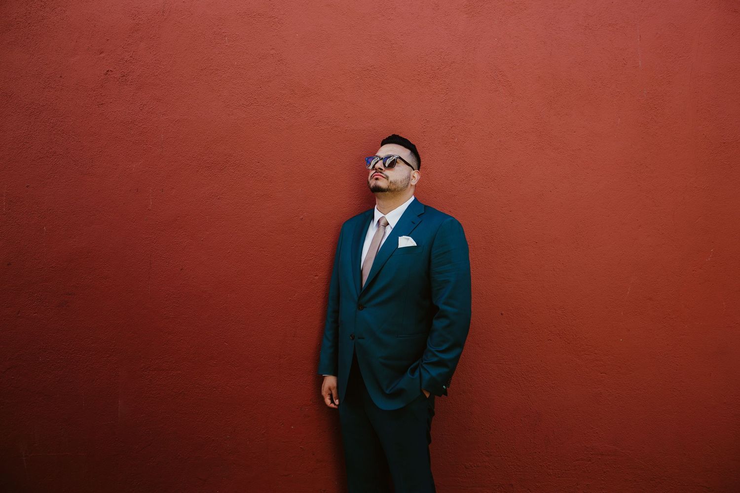 A series of formal portraits against a red background show a person in a black suit and glasses in different poses.