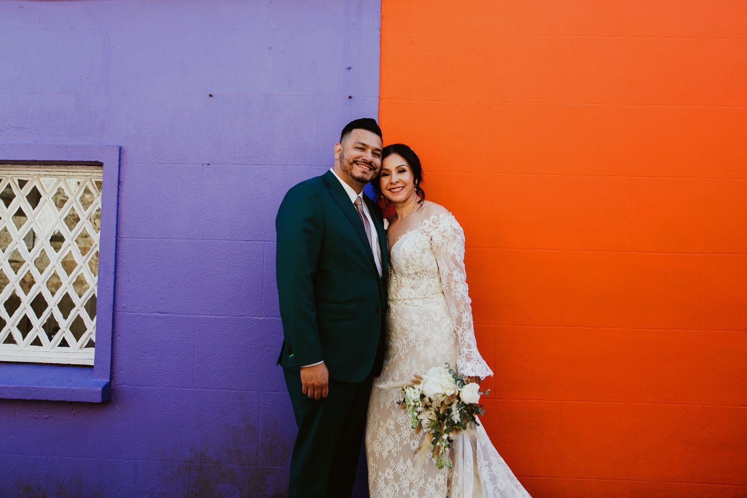 A couple poses for a wedding photo against vibrant orange and purple walls.