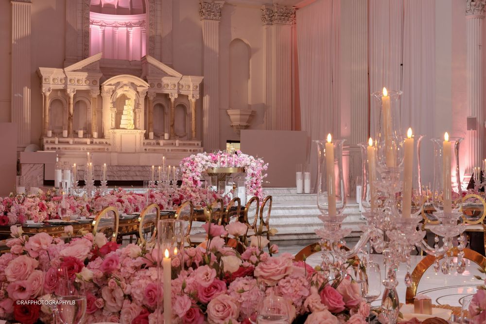 Elegant wedding reception hall decorated with opulent pink floral arrangements and white columns for a luxurious celebration.