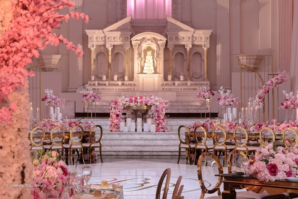 Luxurious indoor wedding ceremony setup with pink florals and cross-back chairs in an ornate church with altar.