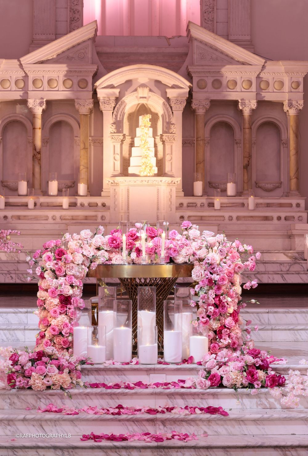 Elegant wedding altar arch decorated with pink roses and candles in front of an ornate white architectural backdrop.