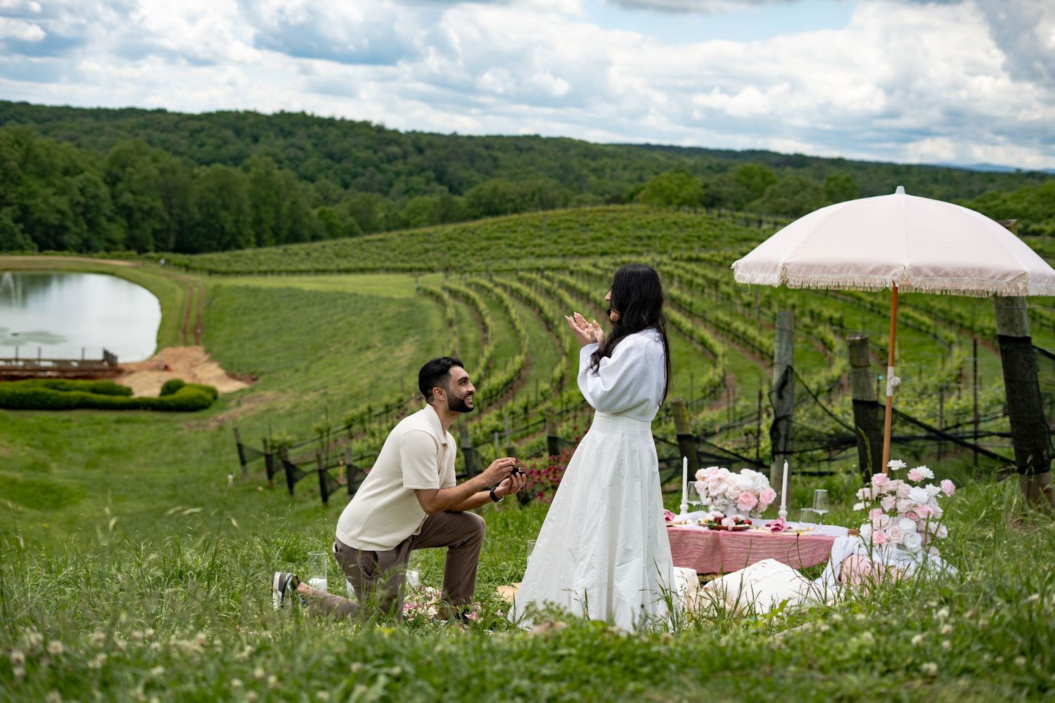 A romantic proposal scene in a picturesque meadow with rolling hills, surrounded by wildflowers and a pink parasol.