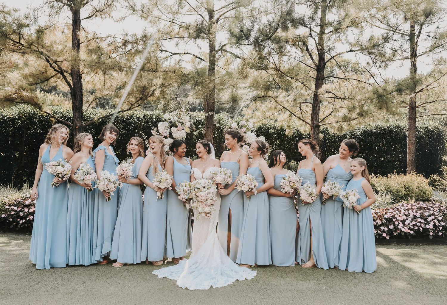 Bridesmaids in powder blue dresses holding bouquets with soft blush roses and eucalyptus