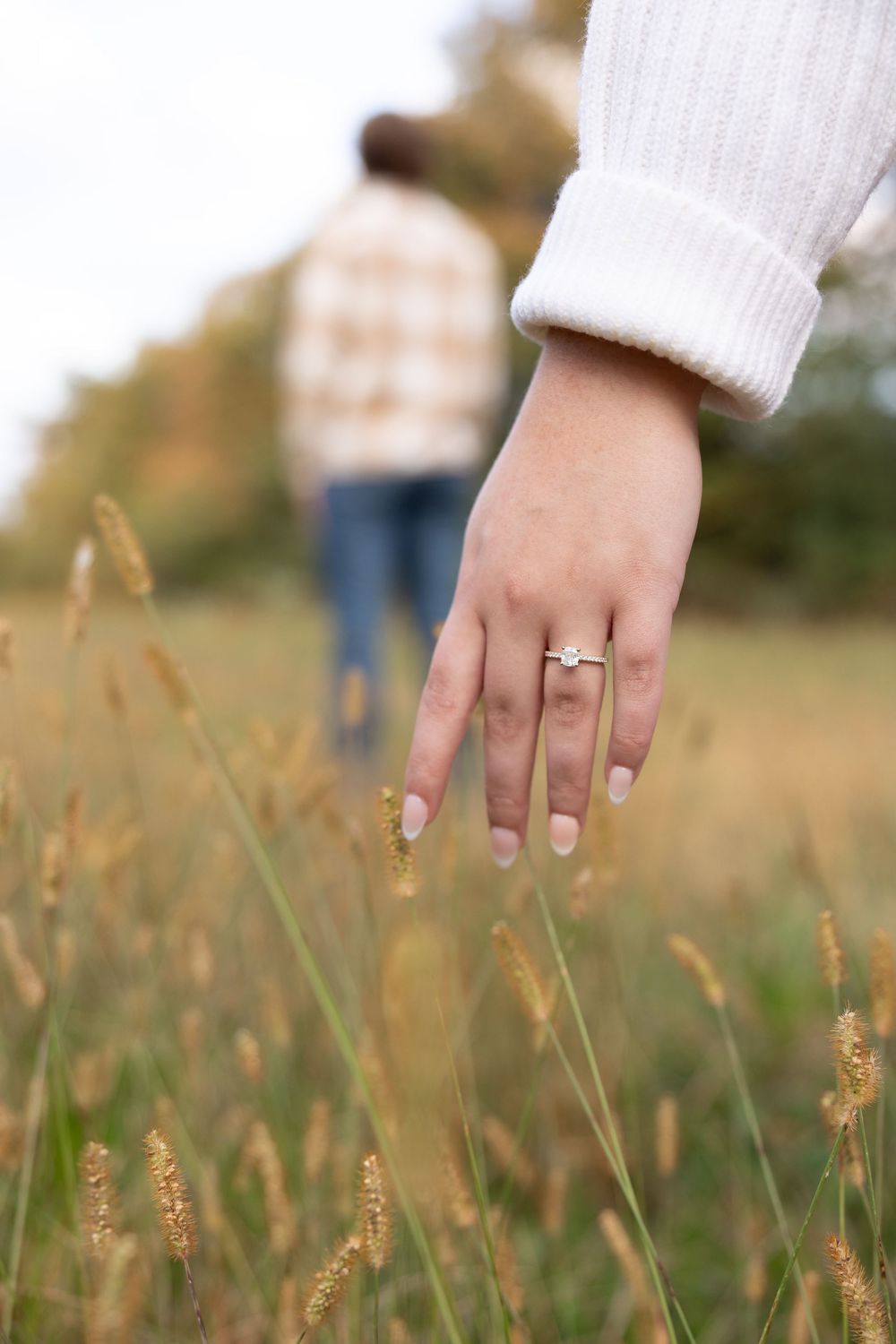 A gold ring glints against dried wheat stalks in a golden field at sunset.