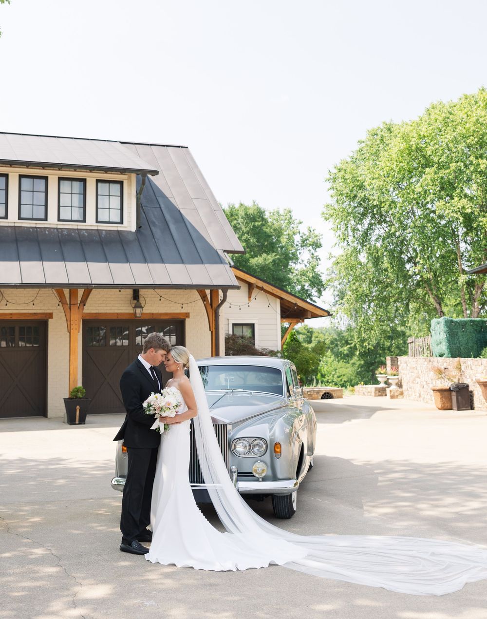 A couple poses together outdoors in front of cars and buildings on a sunny day, creating romantic wedding photos.