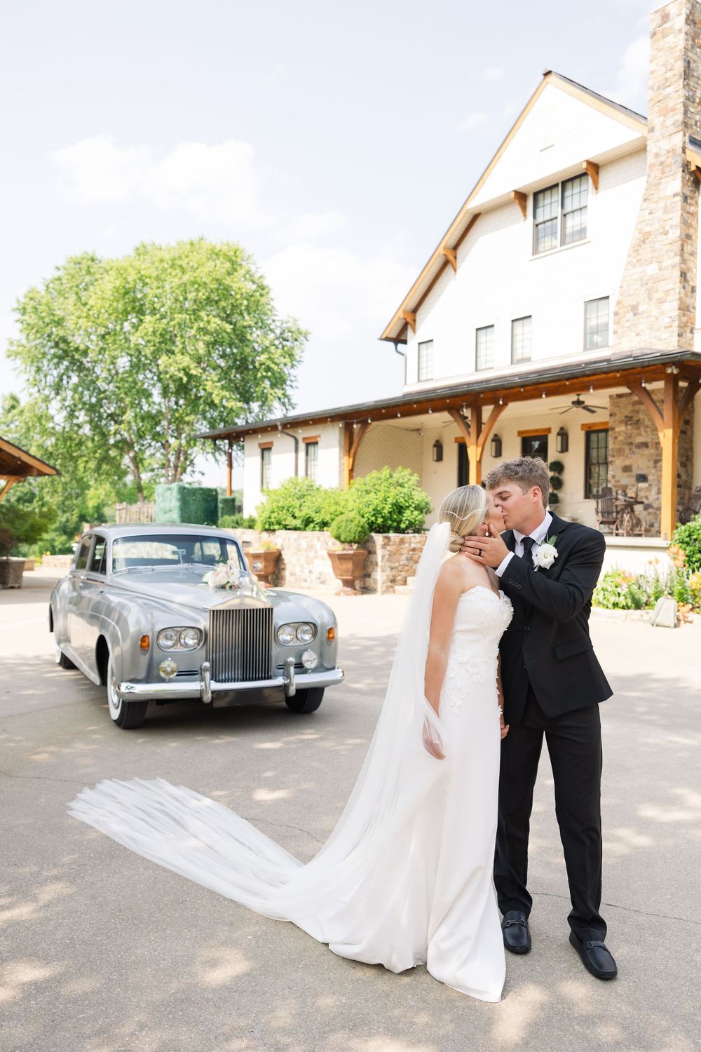 A romantic moment between newlyweds posing next to a vintage Rolls Royce at an elegant outdoor venue.