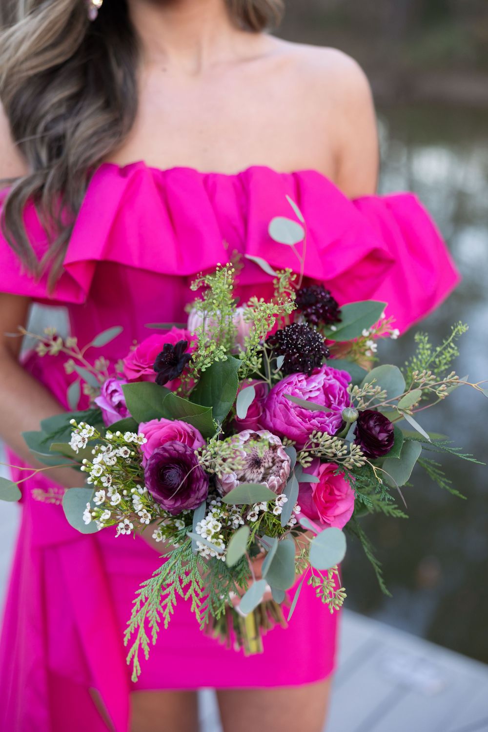A vibrant pink floral bouquet with roses and purple blooms held against a hot pink off-shoulder dress.